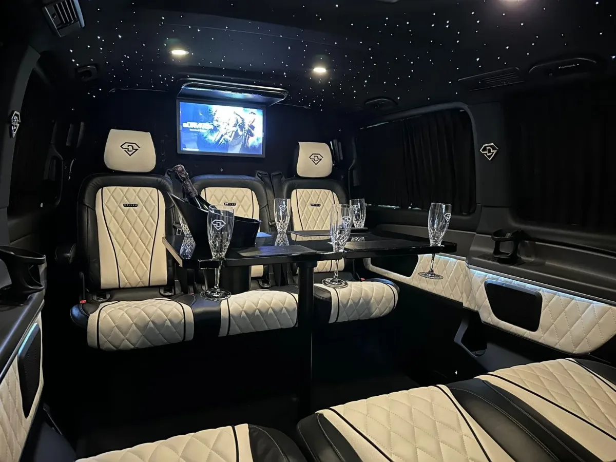 The V-Class cabin: ivory and black quilted leather seats facing across a gloss table, champagne on ice, a screen and a starlit ceiling